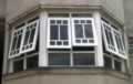 Vista externa de conjunto (baywindow) de janelas maximares com peitoril, bandeira e pinázios.